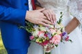 Hands of newlyweds with wedding rings and a bouquet of flowers. The groom in a blue suit and red tie. The concept of Royalty Free Stock Photo