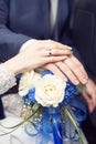 Hands of newlyweds with wedding rings, on a bouquet of white roses with classic blue ribbons. The concept of love and Royalty Free Stock Photo