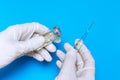 Hands of a nurse in white gloves holding syringe and transparent vial on blue background