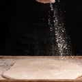 The hands of an old grandmother sprinkle with flour dough