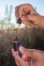 Hands opening CBD oil bottle near hemp plant in a field, close up shot