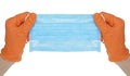 Hands in orange glove holds a blue medical face mask against viruses and bacteria on white background. Protective medical tool