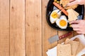 Hands over breakfast plate. Fried egg, wholegrain toast, cheese, hotdog and cup of coffee for breakfast over wooden table, top Royalty Free Stock Photo