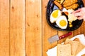 Hands over breakfast plate. Fried egg, wholegrain toast, cheese, hotdog and cup of coffee for breakfast over wooden table, top Royalty Free Stock Photo