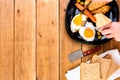 Hands over breakfast plate. Fried egg, wholegrain toast, cheese, hotdog and cup of coffee for breakfast over wooden table, top Royalty Free Stock Photo