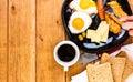 Hands over breakfast plate. Fried egg, wholegrain toast, cheese, hotdog and cup of coffee for breakfast over wooden table, top Royalty Free Stock Photo