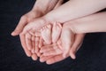 Hands of parents hold the feet of a newborn baby, pink heels in their palms