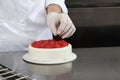 Hands pastry chef prepares a cake, cover with icing and decorate with strawberries, works on a stainless steel kitchen