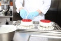 Hands pastry chef prepares a cake, cover with icing and decorate with strawberries, works on a stainless steel industrial kitchen