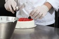 Hands pastry chef prepares a cake, cover with icing and decorate with strawberries, works on a stainless steel kitchen