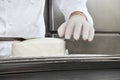 Hands pastry chef prepares a cake, cover pouring white icing, working on a stainless steel kitchen work top