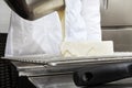 Hands pastry chef prepares a cake, cover pouring white icing, working on a stainless steel kitchen work top