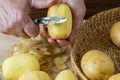 Hands peel potato, peelings on wooden cutting board