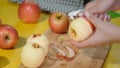 Hands peeling a cooking apple on a wooden board.