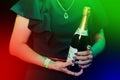 The hands of a person in a black dress and a pendant decoration around his neck hold a bottle of light, sparkling champagne Royalty Free Stock Photo
