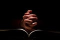 Hands of Person Praying on Top of the Bible