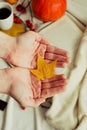 Hands with pine yellow mapleleaf on the background of an autumn still life of a cup of tea pumpkins apples and yellow leaves.