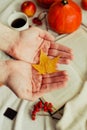 Hands with pine yellow mapleleaf on the background of an autumn still life of a cup of tea pumpkins apples and yellow leaves.