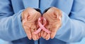 Hands, pink ribbon and breast cancer support with awareness and healthcare icon on blue background. Person in studio Royalty Free Stock Photo