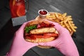 Hands in pink rubber gloves holding burger with pork steak, pickles, fresh vegetabels