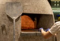 Hands of a pizza maker who puts pizza in the oven using a big shovel. Fire burns Royalty Free Stock Photo