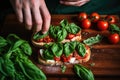 hands placing fresh basil leaves on tomato-covered toast