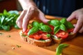 hands placing fresh basil leaves on tomato-covered toast