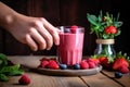 hands placing a glass of berry smoothie on a wooden table