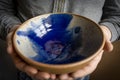 Hands of a potter showing a blue painted clay bowl inside