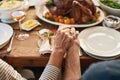 Hands, pray and food with a senior couple sitting at a dining room table for a roast lunch together. Prayer, grace and