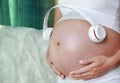 Hands of pregnant woman holding headset putting headphones to belly, motherhood concept