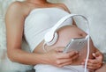 Hands of pregnant woman holding headset putting headphones to belly, motherhood concept