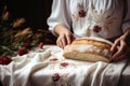 Hands present a loaf of bread on an embroidered cloth.