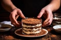 hands pressing down onto tiramisu layers in a dessert bowl