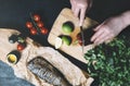 Hands in the process of cooking fish, pepper, parsley, tomato, lime on a cutting board on a black wooden background top view horiz