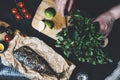 Hands in the process of cooking fish, pepper, parsley, tomato, lime on a cutting board on a black wooden background top view horiz