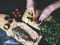 Hands in the process of cooking fish, pepper, parsley, tomato, lime on a cutting board on a black wooden background top view horiz