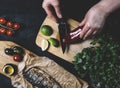 Hands in the process of cooking fish, pepper, parsley, tomato, lime on a cutting board on a black wooden background top view horiz Royalty Free Stock Photo