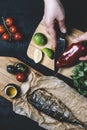 Hands in the process of cooking fish, pepper, parsley, tomato, lime on a cutting board on a black wooden background top view vert