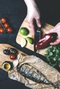 Hands in the process of cooking fish, pepper, parsley, tomato, lime on a cutting board on a black wooden background top view verti Royalty Free Stock Photo