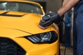 Hands of professional car service worker, with orbital polisher, polishing yellow luxury car hood Royalty Free Stock Photo