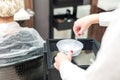 Hands of professional hair stylist are mixing hair dye in a bowl.