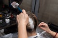 The hands of a professional hairdresser hold the brush in the process of dyeing the hair on the client's head