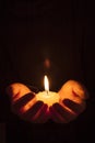 Hands protecting the glowing flame of a candle in the darkness