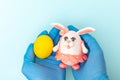 Hands in protective medical gloves holding a painted yellow Easter egg and a homemade Easter bunny Royalty Free Stock Photo