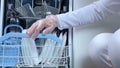 Hands putting white plates in dishwasher. Full loaded dishwasher