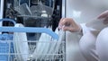 Hands putting white plates in dishwasher. Full loaded dishwasher