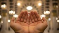 Hands raised in prayer with blurred mosque lights background Royalty Free Stock Photo