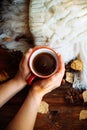 Hands in red knitted gloves holding a hot cup of coffee against yellow leaves background. Concept of autumn time, warmth and cozin