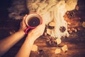 Hands in red knitted gloves holding a hot cup of coffee against yellow leaves background. Concept of autumn time, warmth and cozin